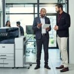 Deux hommes dans un bureau discutent sur une tablette à côté d'une imprimante multifonction couleur Xerox® AltaLink® série C8200 Deux hommes dans un bureau discutent sur une tablette à côté d'une imprimante multifonction couleur Xerox® AltaLink® série C8200