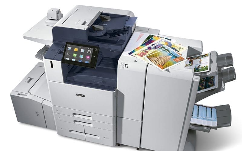 Une imprimante multifonction Xerox moderne et volumineuse, montrant son &eacute;cran tactile et ses multiples bacs de sortie remplis de documents et de tirages couleur de haute qualit&eacute;, symbolisant la performance pour les environnements de bureau exigeants.